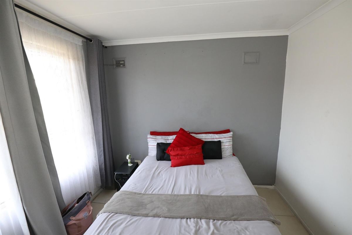 A standard bedroom featuring tiled flooring, a neutral grey accent wall, and a large window allowing for natural light.