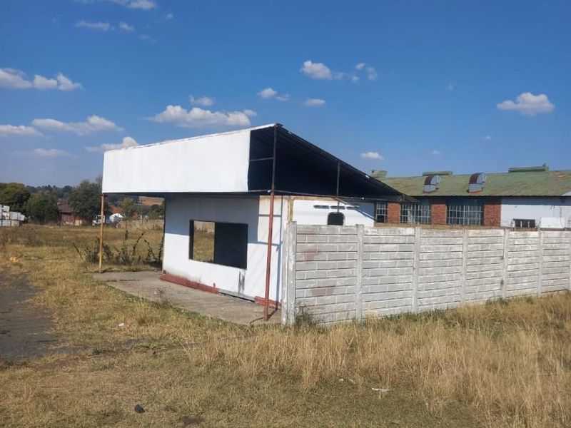 A view of a small, detached structure on a vacant residential lot, featuring a simple roof canopy and concrete block perimeter walling.