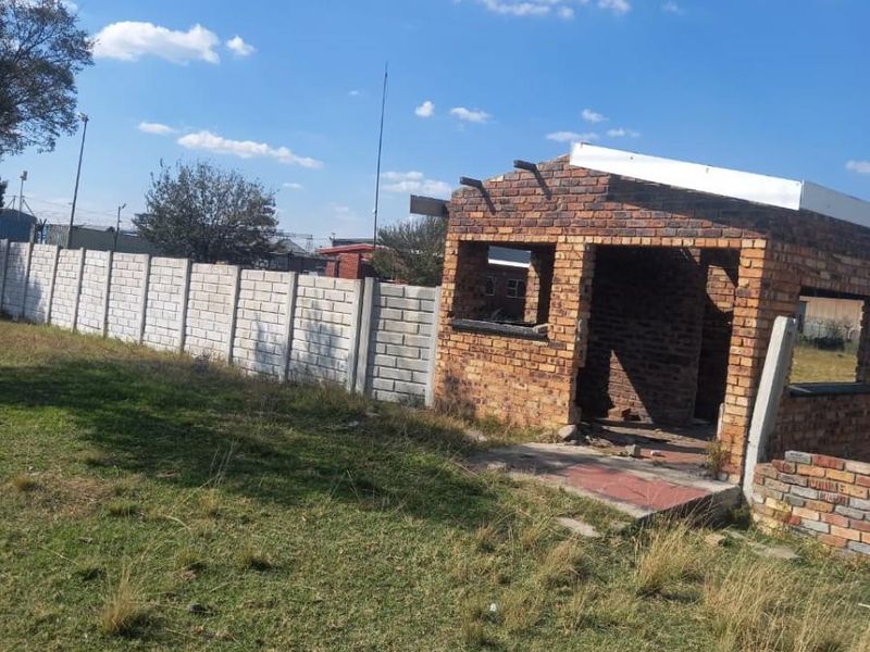A view of a residential plot featuring an unfinished brick structure and perimeter walling, offering potential for development or completion.