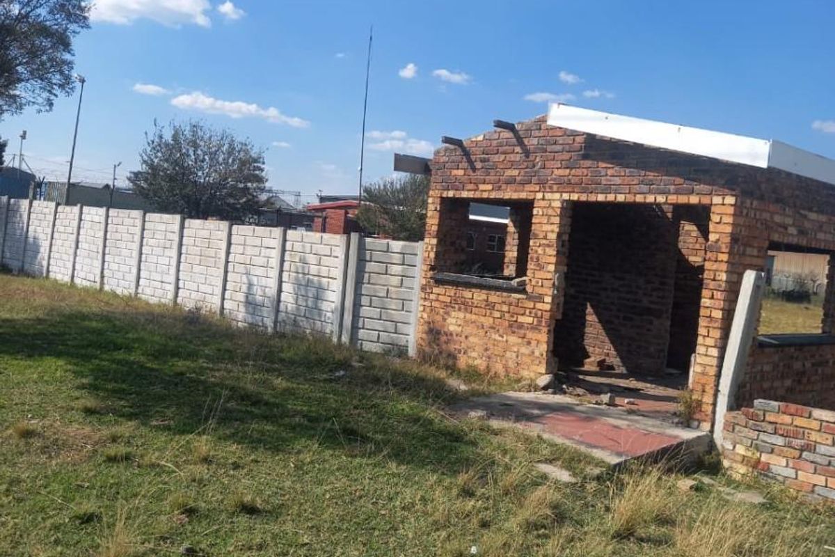 A view of a residential plot featuring an unfinished brick structure and perimeter walling, offering potential for development or completion.