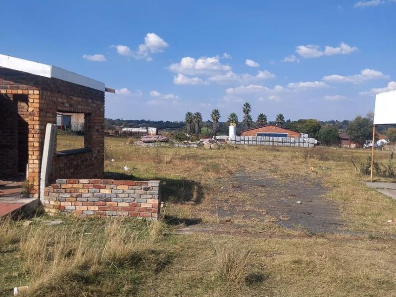A view of a vacant residential plot featuring an unfinished brick structure and expansive open land with natural grass coverage.