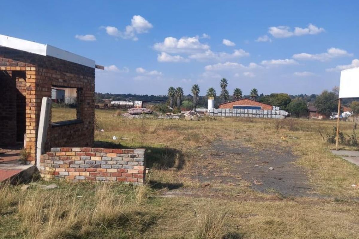 A view of a vacant residential plot featuring an unfinished brick structure and expansive open land with natural grass coverage.