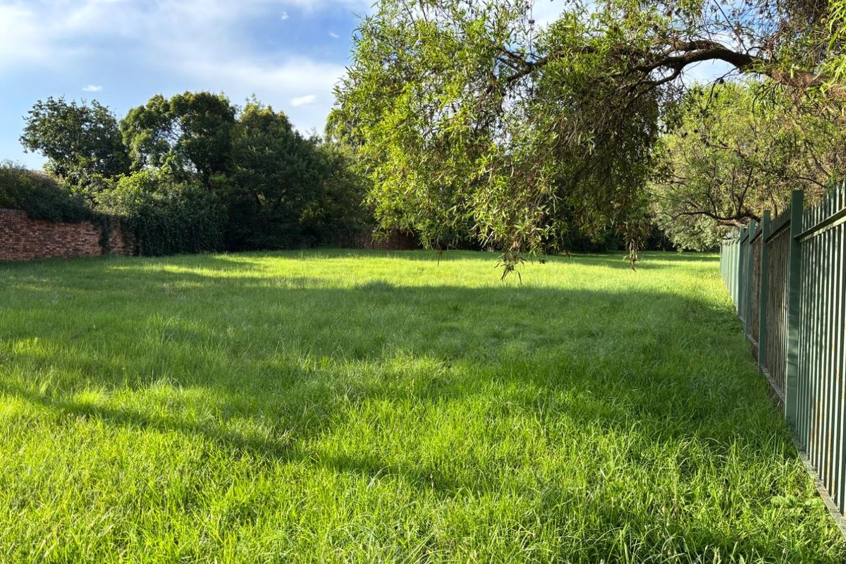 A spacious, level residential vacant land plot featuring established trees, a perimeter brick wall, and secure metal fencing.