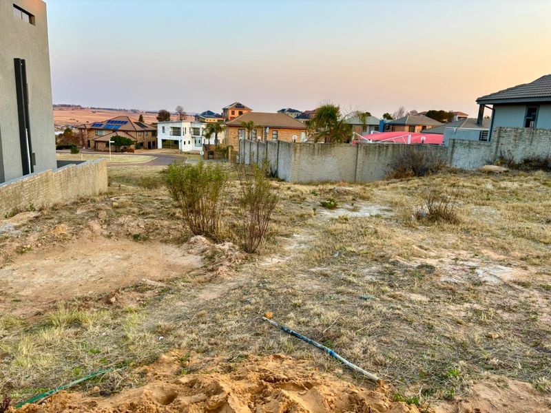 A view of a vacant residential plot featuring natural ground cover and surrounding boundary walls in a developed neighborhood.