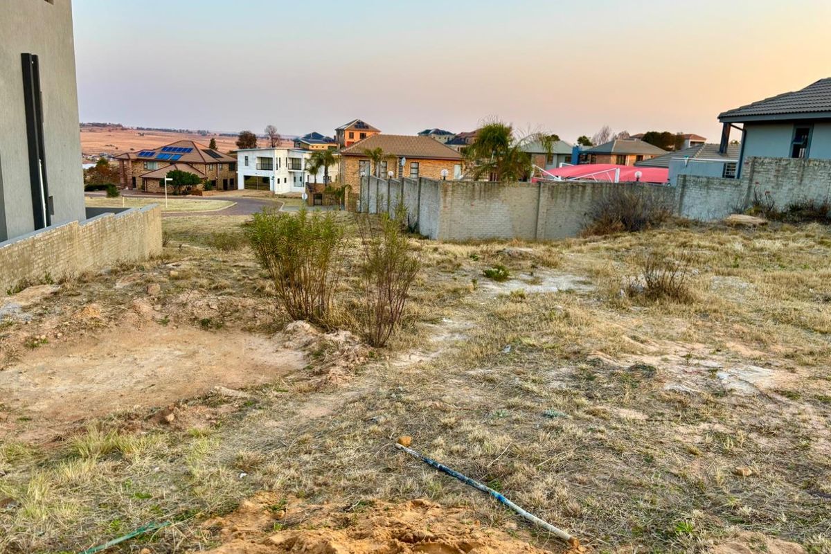 A view of a vacant residential plot featuring natural ground cover and surrounding boundary walls in a developed neighborhood.