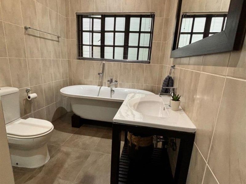 A well-maintained bathroom featuring a freestanding bathtub, a modern vanity basin, and neutral floor-to-ceiling wall tiles.