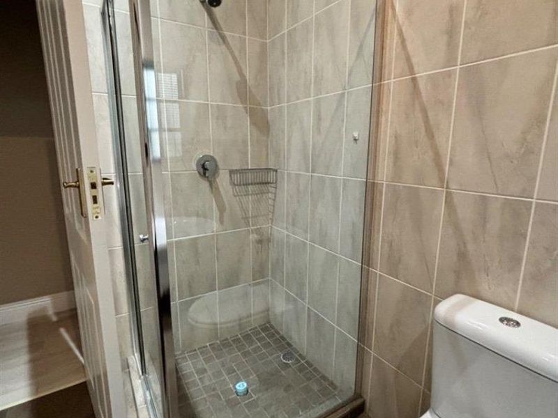 A functional bathroom featuring a glass-enclosed shower with tiled walls and a standard toilet, finished with neutral ceramic tiling.
