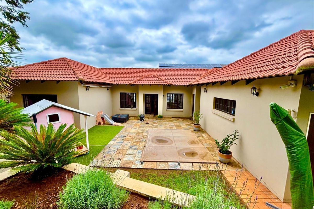A well-maintained rear courtyard featuring a stone-paved patio, swimming pool with cover, and terracotta tiled roof, providing a functional outdoor living space.