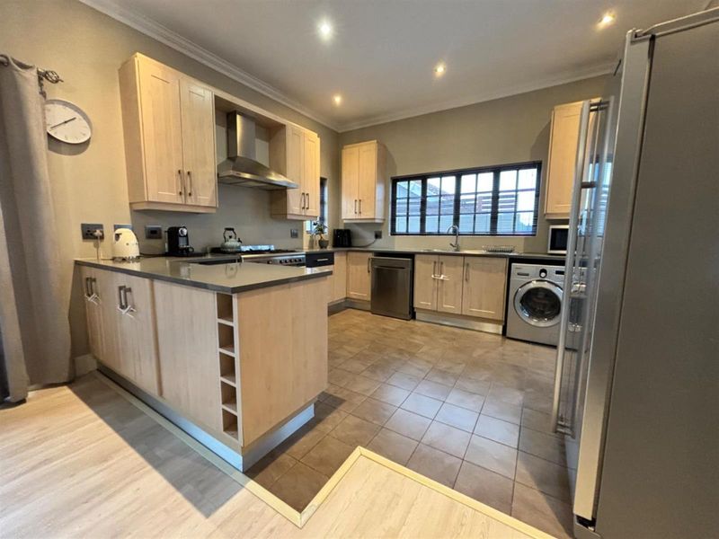 A functional kitchen featuring light wood cabinetry, stone countertops, integrated stainless steel appliances, and tiled flooring with recessed lighting.