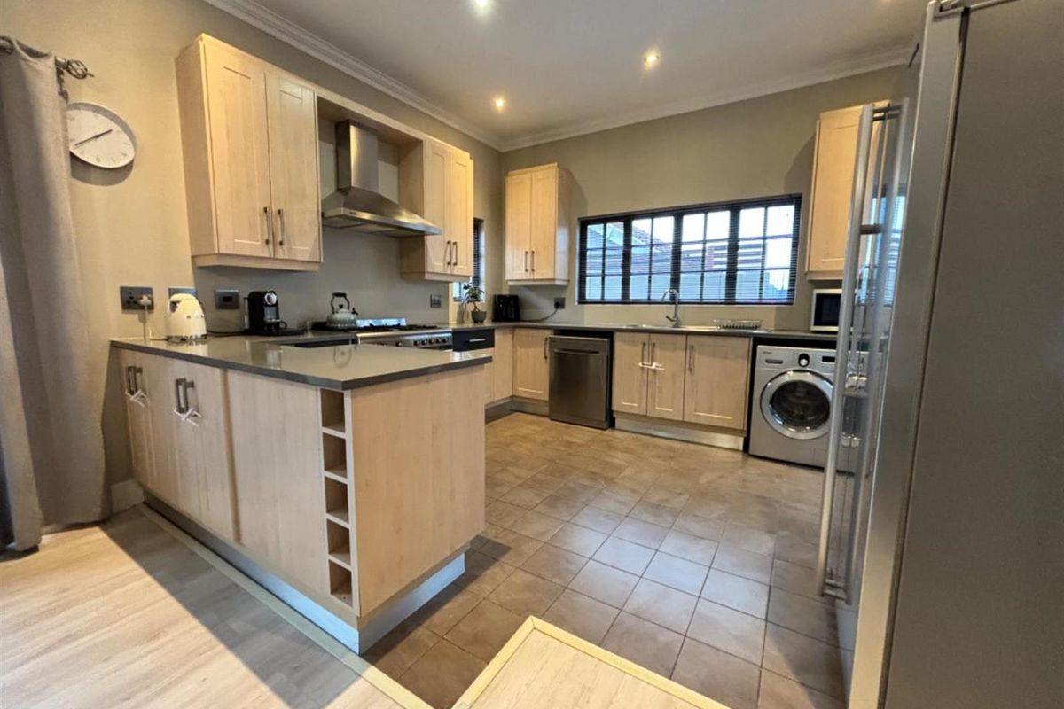 A functional kitchen featuring light wood cabinetry, stone countertops, integrated stainless steel appliances, and tiled flooring with recessed lighting.
