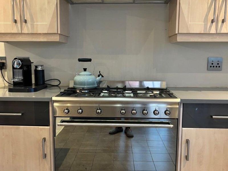 A functional kitchen featuring a stainless steel gas stove, matching extractor fan, stone countertops, and light wood-finish cabinetry.