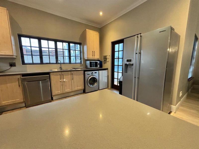 A functional kitchen featuring light wood cabinetry, stone countertops, integrated appliances, and direct access to the exterior via a glass-paneled door.