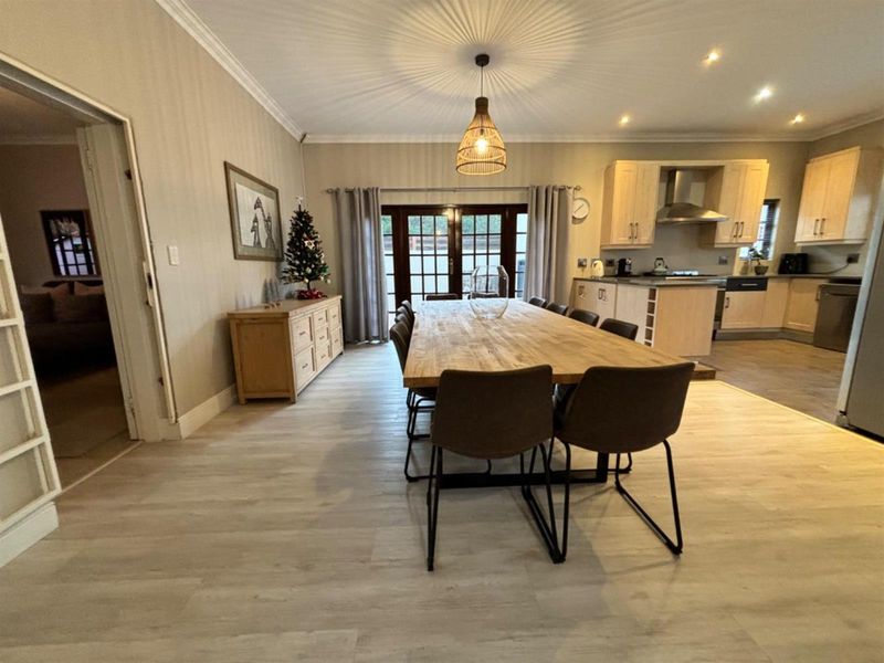 Spacious open-plan dining and kitchen area featuring light wood cabinetry, modern laminate flooring, and direct access to the outdoor area through french doors.