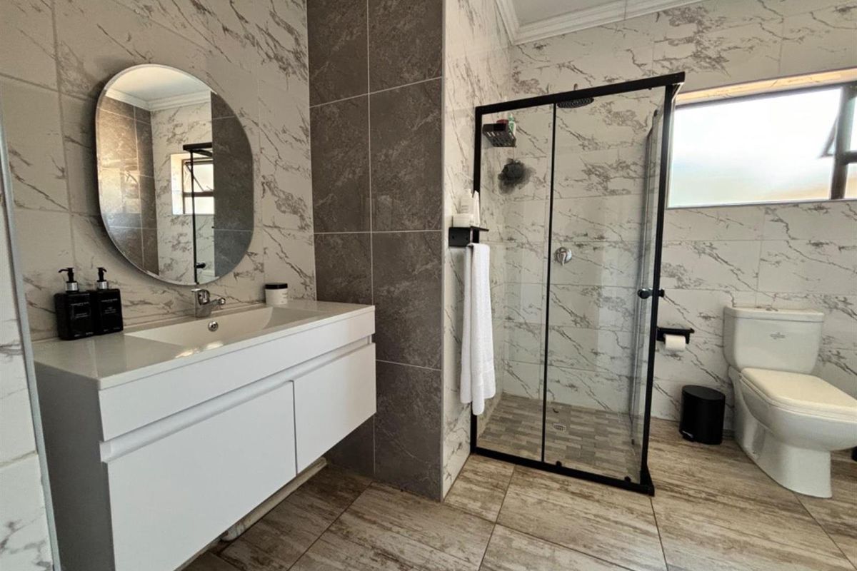 Modern bathroom featuring a floating vanity, glass-enclosed shower with rain shower head, and contemporary marble-effect wall tiling.