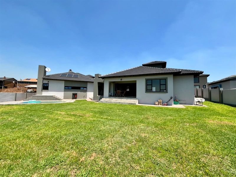 Rear view of the property featuring a spacious lawn, swimming pool, concrete patio area, and modern tiled roof with solar panels.