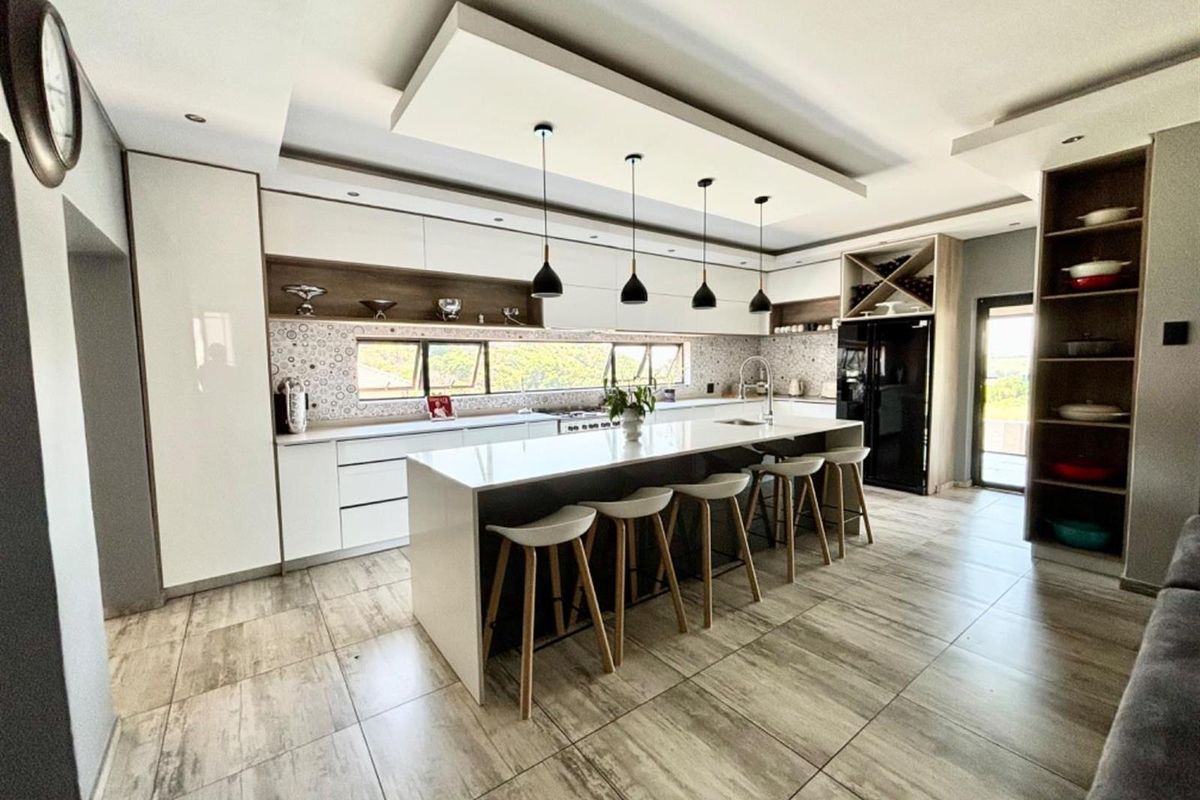 Modern kitchen featuring a large central island with stone countertops, sleek built-in cabinetry, patterned backsplash, and contemporary pendant lighting.