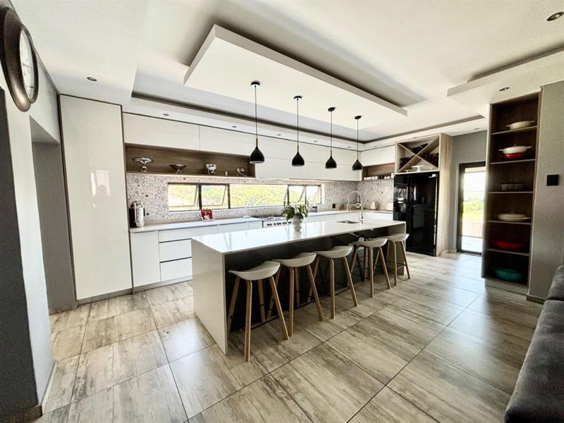 Modern kitchen featuring a large central island with stone countertops, sleek built-in cabinetry, patterned backsplash, and contemporary pendant lighting.