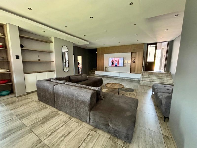 Spacious living room featuring modern tiled flooring, recessed ceiling lights, and custom built-in media cabinetry with timber slat wall detailing.