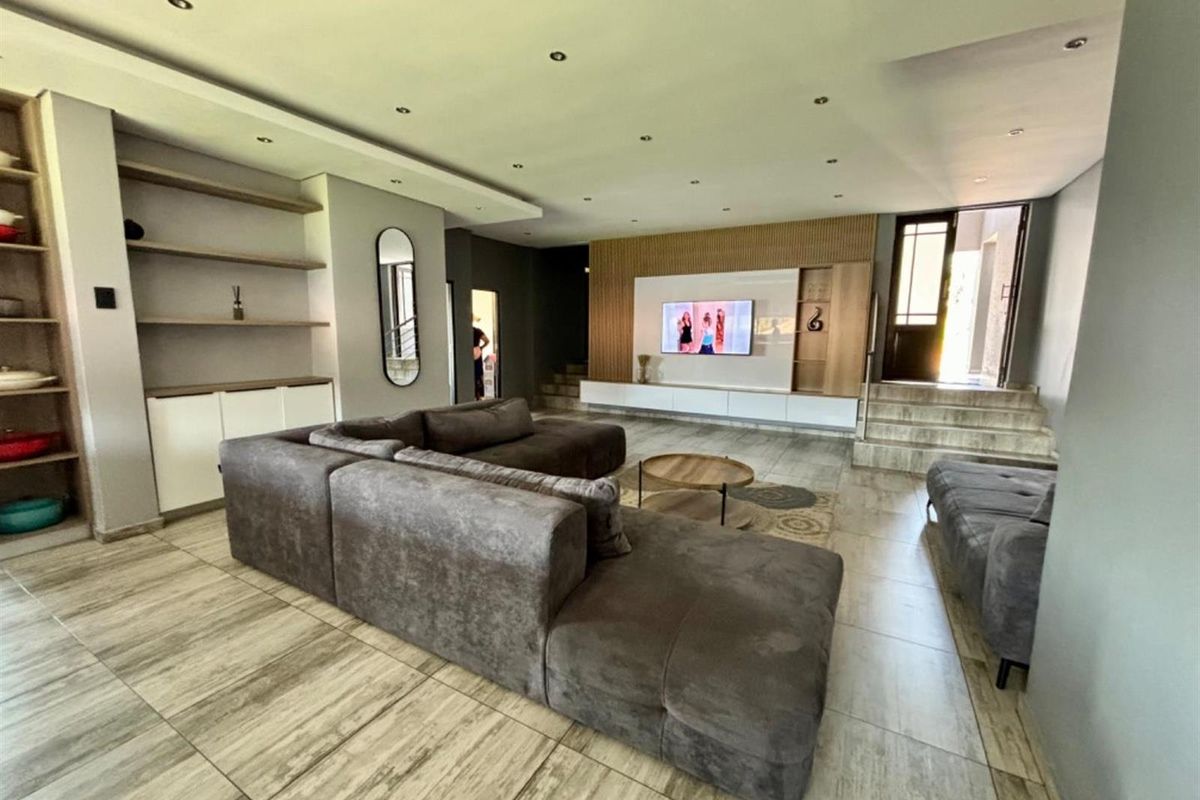 Spacious living room featuring modern tiled flooring, recessed ceiling lights, and custom built-in media cabinetry with timber slat wall detailing.