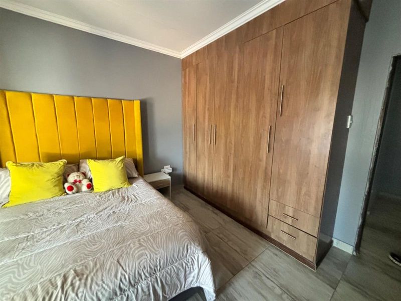 A well-maintained bedroom featuring extensive floor-to-ceiling built-in wooden wardrobes, modern tiled flooring, and decorative crown molding.