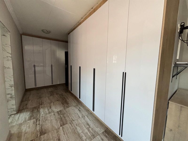 A spacious hallway featuring extensive floor-to-ceiling built-in cabinetry with modern white finishes and wood-look tiled flooring.