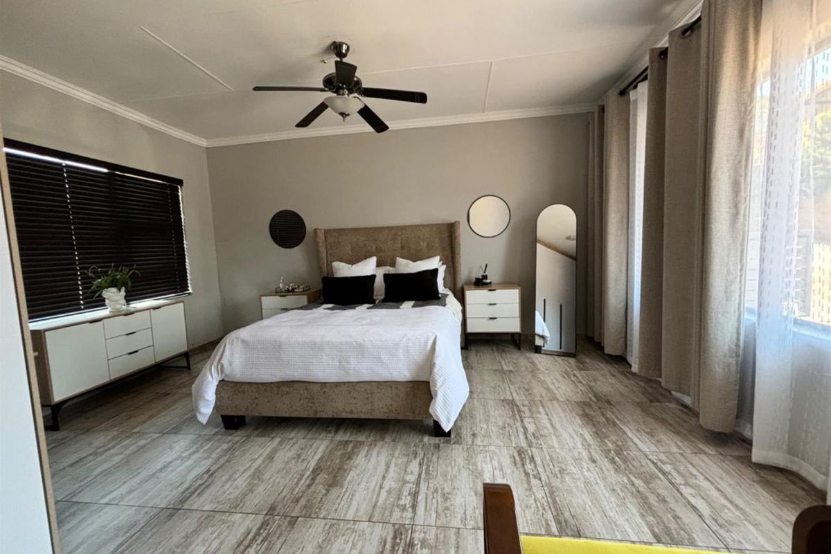 Spacious bedroom featuring wood-look tile flooring, a ceiling fan, and large windows with fitted blinds and curtains.