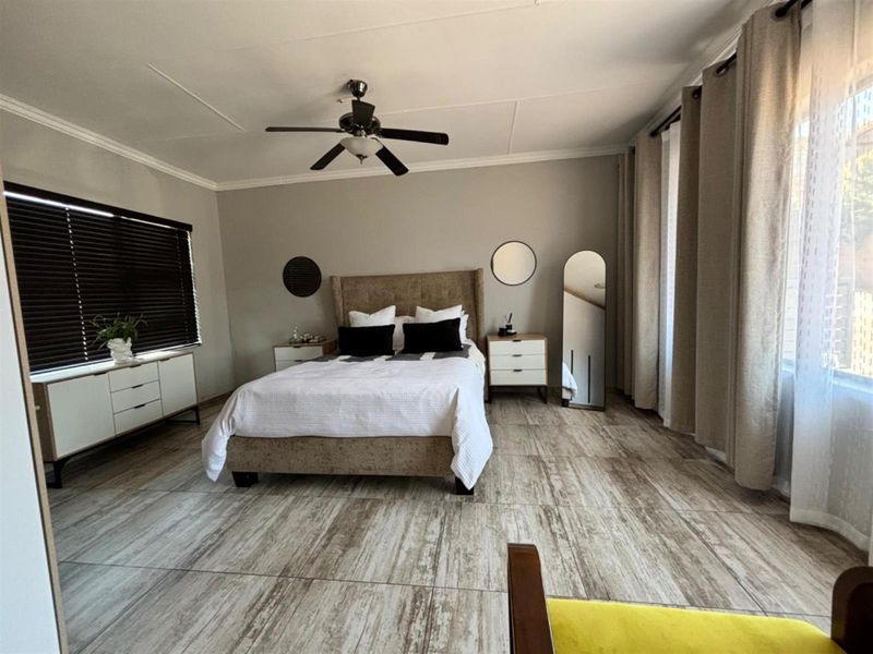 Spacious bedroom featuring wood-look tile flooring, a ceiling fan, and large windows with fitted blinds and curtains.