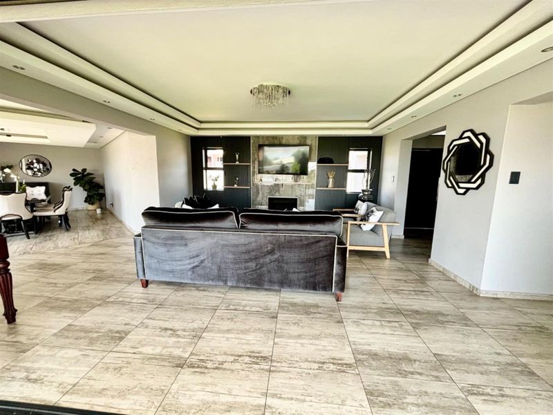 Spacious living room featuring a modern recessed ceiling, built-in fireplace with integrated shelving, and neutral tiled flooring throughout.