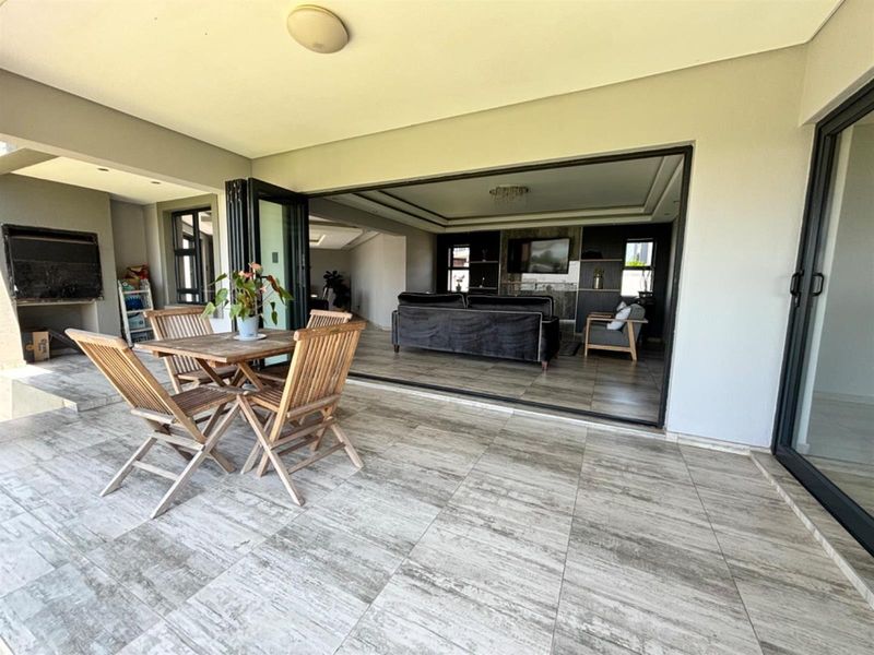 Covered patio featuring large format floor tiles, a built-in braai, and seamless stacking doors providing direct access to the open-plan living area.