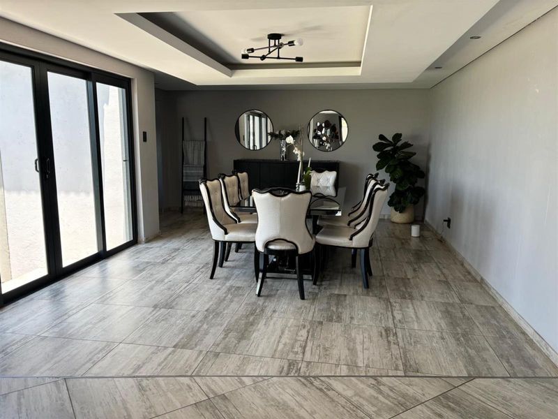 Spacious dining room featuring modern tiled flooring, a recessed ceiling with contemporary lighting, and large sliding glass doors providing natural light.