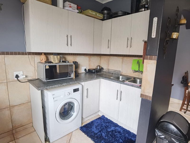 Compact scullery area featuring light wood-grain cabinetry, granite countertops, a double stainless steel sink, and dedicated space for a washing machine.
