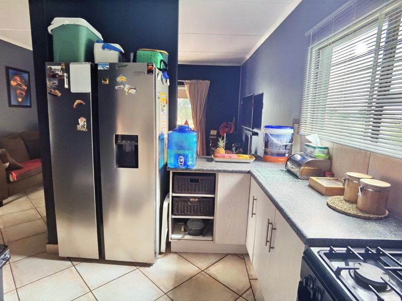 A functional kitchen featuring laminate cabinetry, stone-look countertops, a gas hob, and tiled flooring, with a window providing natural light.