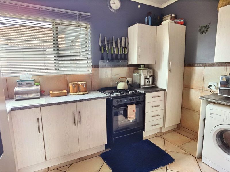 A functional kitchen featuring light-toned laminate cabinetry, stone-look countertops, a gas stove with oven, and tiled flooring with a neutral backsplash.