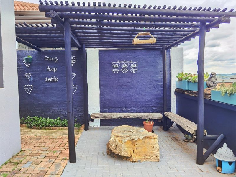 Outdoor patio area featuring a timber pergola structure, brick paving, and built-in timber bench seating against a painted feature wall.