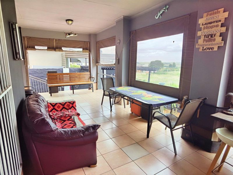 A covered patio area featuring tiled flooring and large windows with roll-up canvas blinds, offering views of the surrounding landscape.