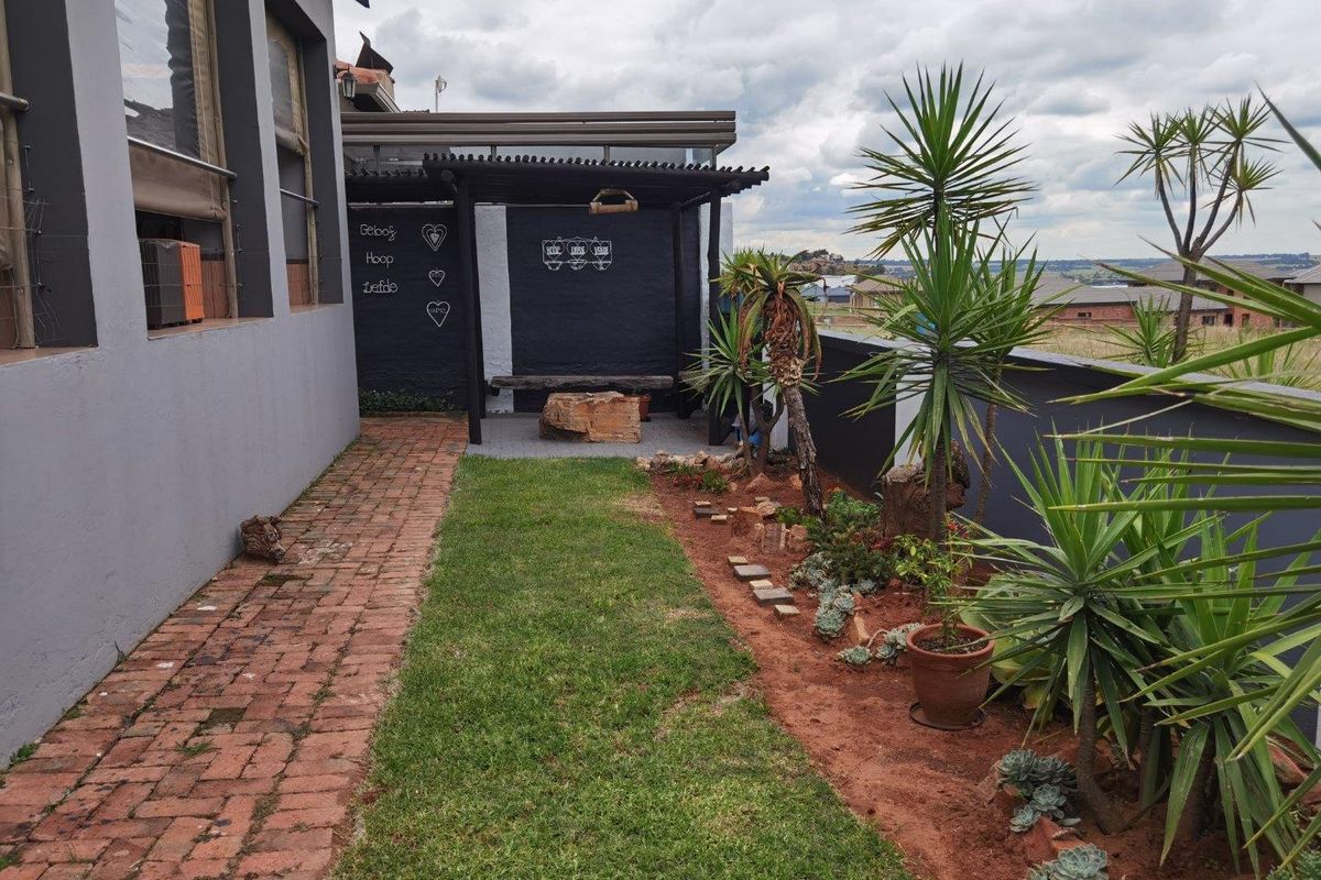 A well-maintained rear garden area featuring a brick-paved pathway, a covered pergola structure, and landscaped garden beds with established plants.