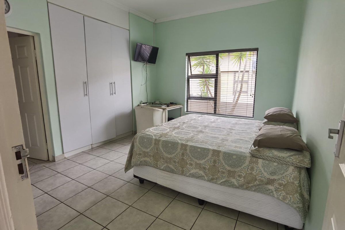 A functional bedroom featuring built-in cupboards, tiled flooring, and a window fitted with horizontal blinds.