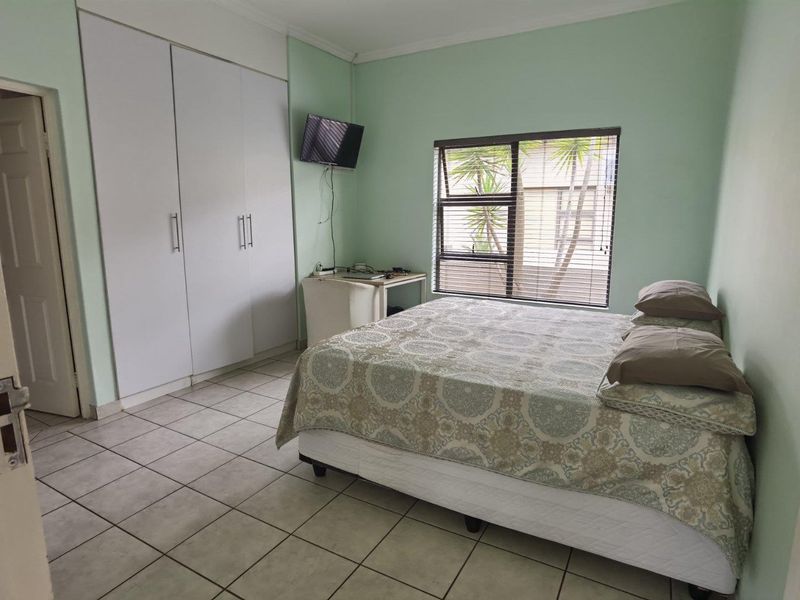 A functional bedroom featuring built-in cupboards, tiled flooring, and a window fitted with horizontal blinds.