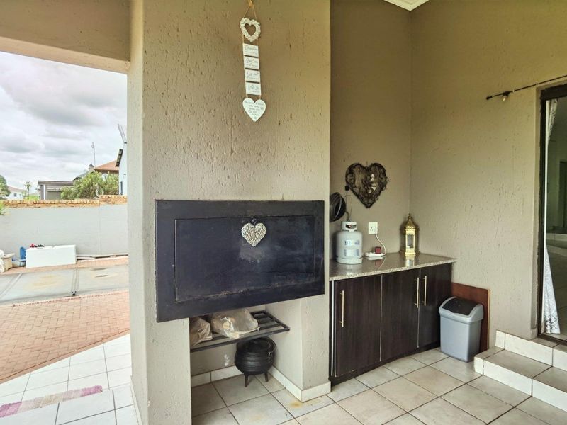 Covered patio area featuring a built-in braai, granite-topped cabinetry, and tiled flooring, providing a functional outdoor entertainment space.