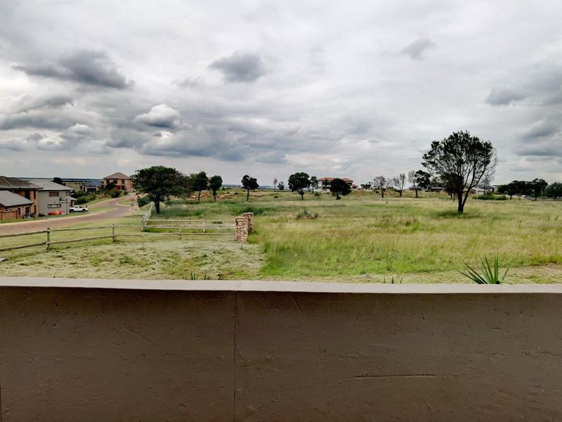 An elevated view from a balcony overlooking an open field and surrounding residential neighborhood.