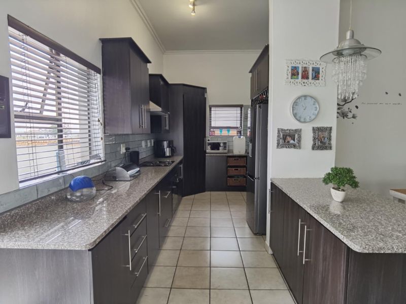 Modern kitchen featuring dark wood cabinetry, granite countertops, tiled flooring, and a functional layout with integrated appliances and ample storage space.