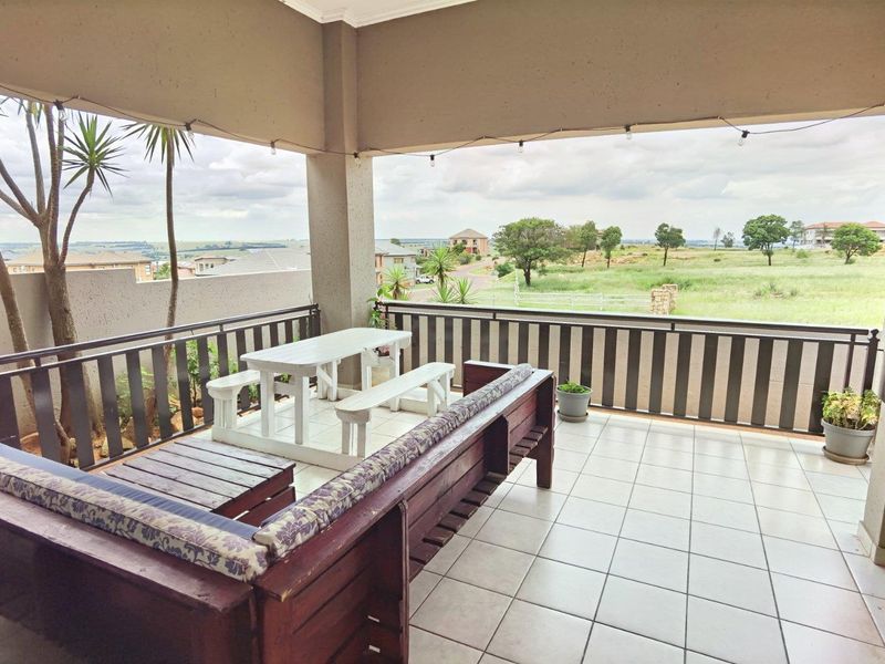A spacious covered patio featuring tiled flooring and a metal balustrade, offering expansive views of the surrounding landscape.