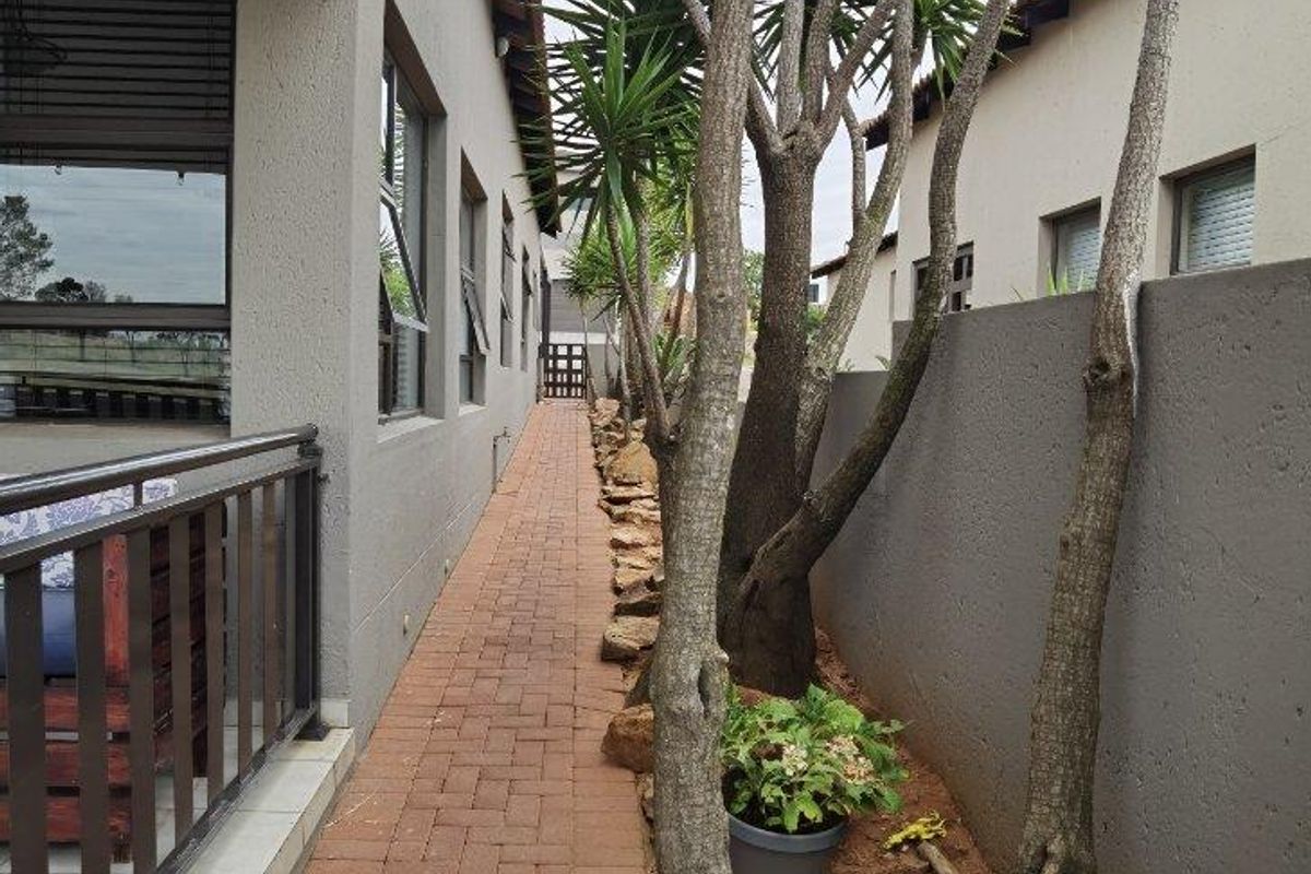 A side walkway featuring brick paving, a solid boundary wall, and mature trees, providing a clean and functional outdoor passage along the side of the house.