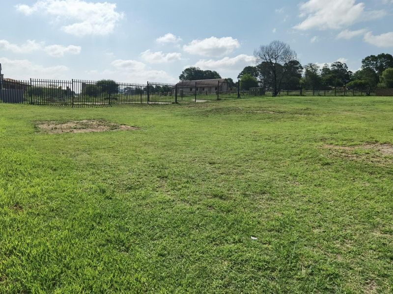 A spacious, level residential vacant land plot featuring established grass lawn and secure metal perimeter fencing.