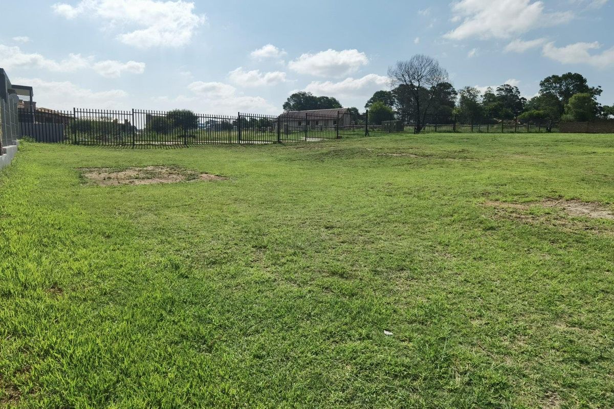 A spacious, level residential vacant land plot featuring established grass lawn and secure metal perimeter fencing.