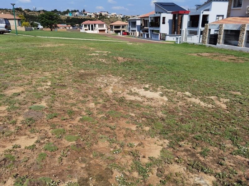 A vacant residential plot of land featuring a grass lawn with surrounding neighborhood housing developments.