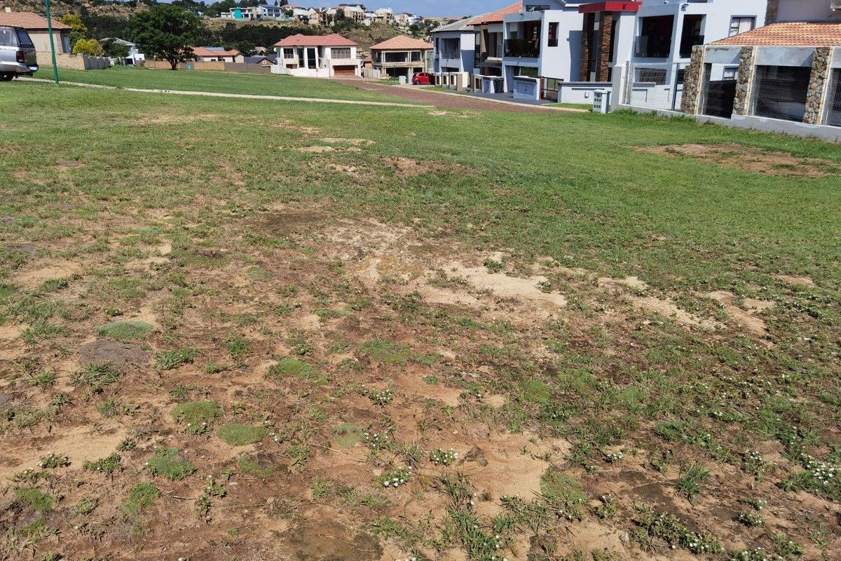 A vacant residential plot of land featuring a grass lawn with surrounding neighborhood housing developments.