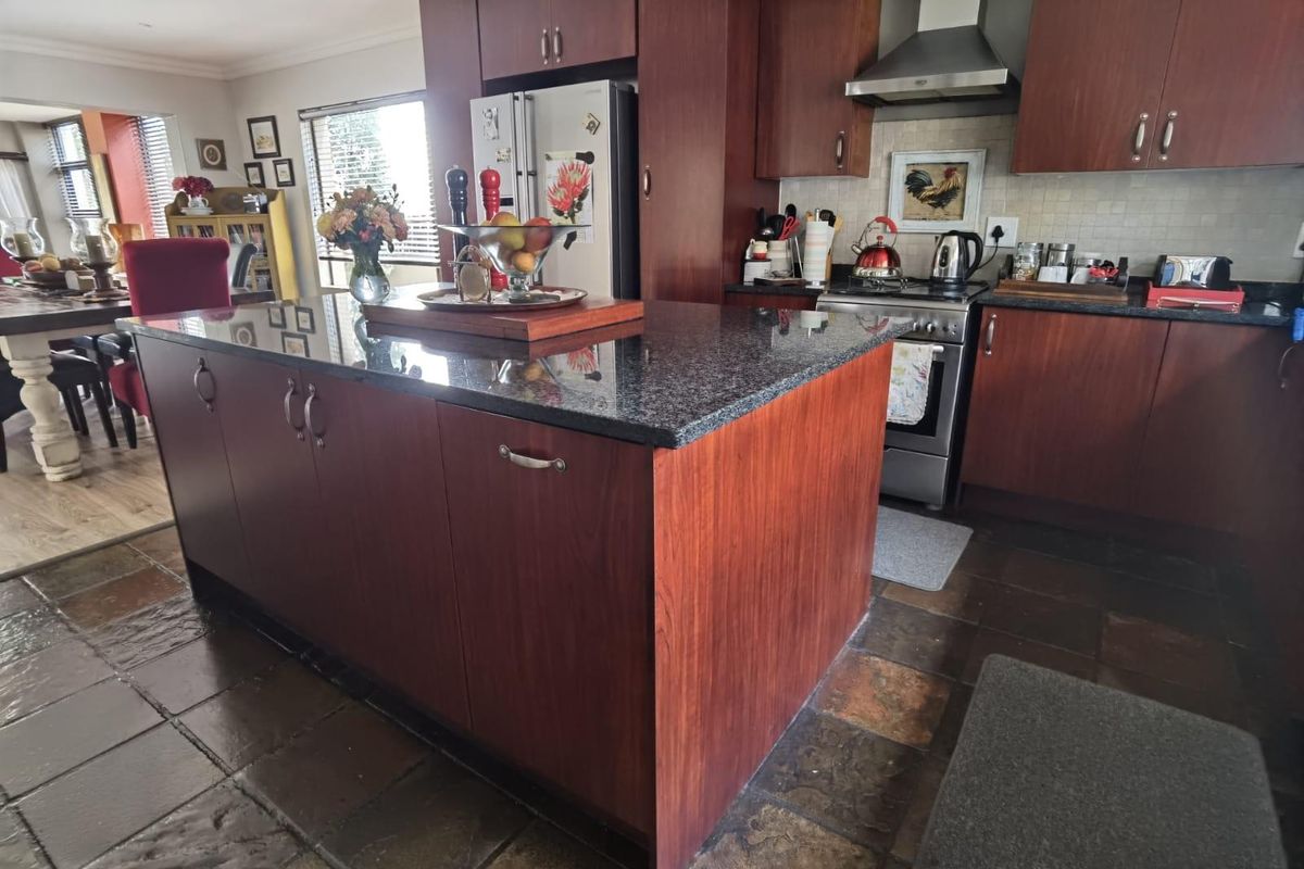A functional kitchen featuring dark wood cabinetry, granite countertops, a central island, and tiled flooring, seamlessly flowing into the adjacent dining area.