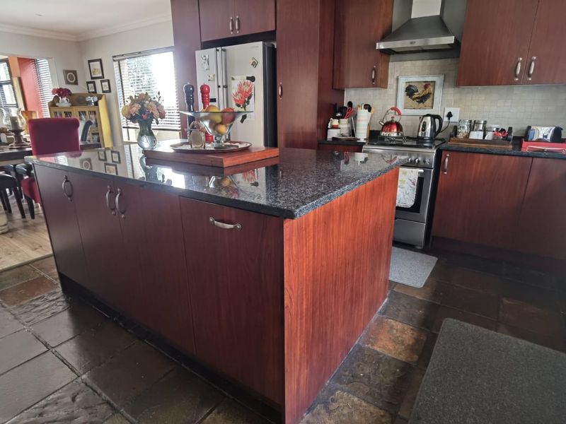 A functional kitchen featuring dark wood cabinetry, granite countertops, a central island, and tiled flooring, seamlessly flowing into the adjacent dining area.