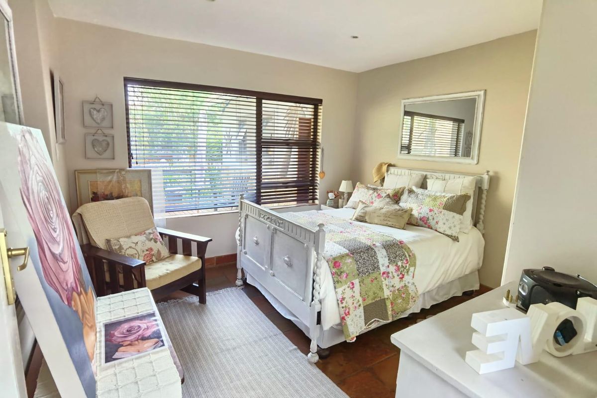 A cozy bedroom featuring terracotta floor tiles, recessed downlighting, and large windows fitted with venetian blinds.